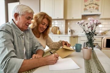 Woman with envelope looking at man writing letter