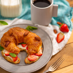 Nicely set breakfast table. Appetizing croissant with strawberries. almonds, mint leaves, a cup of black coffee, milk on a light background. Advertising, banner.