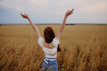 red-haired woman with raised up hands in the field back view