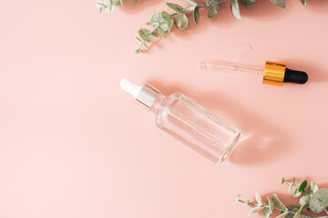 Glass bottle with pipettes on pink background with home flower.