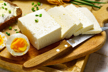 tasty lunch in rural style, healthy food - sliced feta cheese, eggs, bread and butter sandwich, green leek and rye bread, cooked food on a white wooden boards