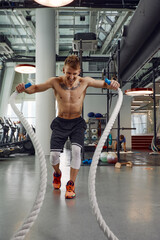 Front view of Attractive young fit and toned sportswoman working out with battle ropes. Motion blur