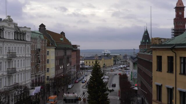 Aerial of Helsingborg in Scania, Sweden scenic coastal city with historic European style buildings with boat ferry cruise moving in water, cars driving and turning on the streets, people crossing road