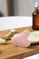 Jade and rose quartz gua sha tools, natural face roller with cosmetic product on wooden bath caddy, closeup