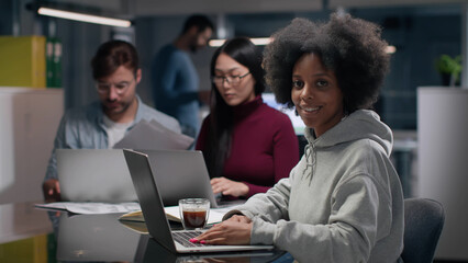 Obraz premium Portrait of African-American woman working on laptop and smiling at camera in office 