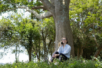 Fototapeta premium Young woman using a smartphone at day time with a green park in the background. High quality photo