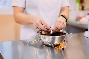 A pastry chef crumbles a chocolate sponge cake into a metal bowl to make a potato cake later
