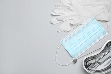 Set of different dentist's tools, face masks and gloves on light grey background, flat lay. Space for text