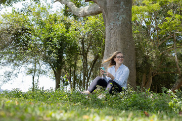 Young woman using a smartphone at day time with a green park in the background. High quality photo