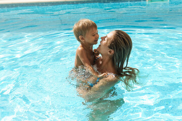 Fototapeta na wymiar Mother and her cute little son swimming in outdoor pool during summer vacation