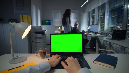 Pov shot of businessman typing on laptop with green screen late in office - obrazy, fototapety, plakaty