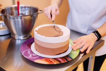 The pastry chef spreads chocolate cream on the cake. The cake consists of three layers of chocolate: white, milky and dark