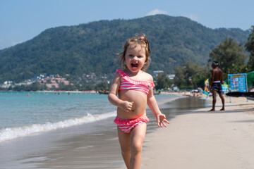 a little girl with curly hair is playing, laughing, rejoicing on the seashore. a child is playing on a sandy beach. happy childhood. summer holidays. kids and the sea