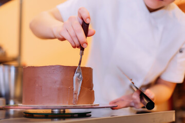 Fototapeta na wymiar The pastry chef spreads chocolate cream on the cake. The cake consists of three layers of chocolate: white, milky and dark 