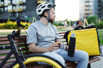 Express delivery courier sitting on bench with thermos and cup of coffee.