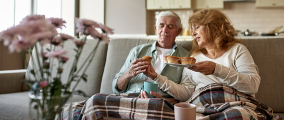 Woman giving cupcake to her husband on sofa