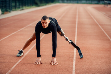 A runner with artificial leg warming up at stadium on running track.