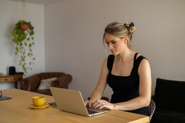 Young woman working at home in her kitchen with laptop and papers on kitchen wooden desk. Home office concept.