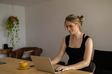 Young woman working at home in her kitchen with laptop and papers on kitchen wooden desk. Home office concept.