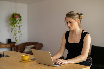 Young woman working at home in her kitchen with laptop and papers on kitchen wooden desk. Home office concept.
