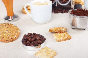 Still life with crackers, cookies, cup of coffee, coffee beans and ground coffee on table.