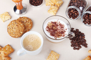 Breakfast with cup of espresso, cappuccino with chocolate crumbs, cookies, crackers and coffee beans on table.