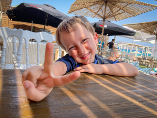 Little boy showing victory sign beside table