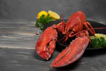 Lobster decorated with lemon slices on black plate on wooden table. Fresh seafood.