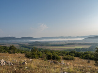 
Morning landscape. View from the mountain to the valley and the village. Sunrise. Fog creeps along the ground in the valley. Blue sky. Mountain landscape.