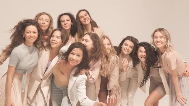 Group of happy women smiling, hugging, having fun in studio. Slow motion, pastel, natural and beige concept.