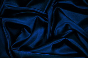 Black blue silk satin. Wavy folds. Shiny fabric surface. Elegant navy blye background with space for design.