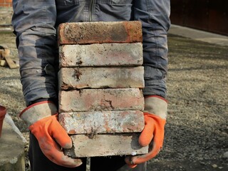 a stack of old bricks in the hands of a hard worker in rubber gloves, dismantling old brickwork for...