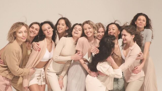 Group of happy women smiling, hugging, having fun in studio. Slow motion, pastel, natural and beige concept.
