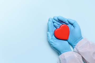 Two hands of a doctor in medical gloves hold a red heart for concept doctors treat and care for patients with heart or cardiology heart disease.Donation concept. Copy space