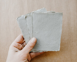 Hand holding white ragged edge art papers with brown paper wood blank background in style shot art studio