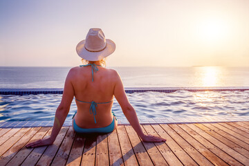 Woman enjoying beach vacation holidays, relaxing at infinity swimming pool of luxury resort hotel,...