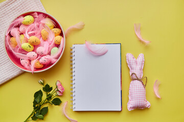 Easter notepad mock up. Pink bowl with colorful eggs, pink feathers and pink rose. Happy Easter concept. Top view. Post card mock up on yellow background