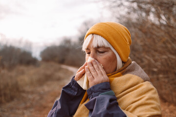 Ill young woman caught cold sneezing in paper tissue at fall city park. Sick allergic female blowing wiping running nose got flu sinusitis coughing, having seasonal allergy symptoms - obrazy, fototapety, plakaty