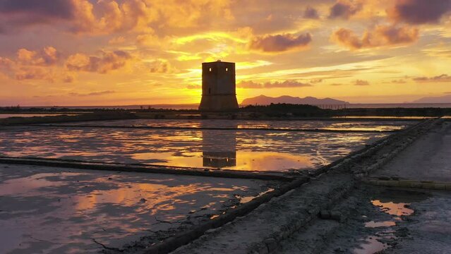 Aerial view over a tower at a salt production brine, sunset in Trapani, Sicily - rising, drone shot