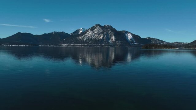 Lake Walchensee in Bavaria, south Germany in the scenic alps mountains close to Austria. Blue clear drinking water waves at the white shore and blue sky in winter. 4K UHD drone aerial.