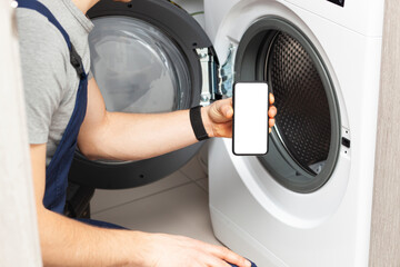 White blank screen on phone in repairman hand who has come to repair the washing machine. Smartphone mockup with empty space. Place for text on phone screen.