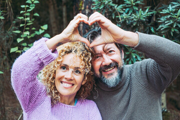 Happy adult couple people in love do hearth symbol gesture with hands together smiling and enjoying...