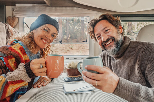 Cheerful adult couple smile and enjoy travel camper van holiday vacation together clinking with cups inside. Happy people tourist posing for a picture indoor. Vanlife lifestyle in the nature