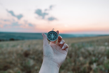 Travel compass in tourist hand on wheat field background at sunset