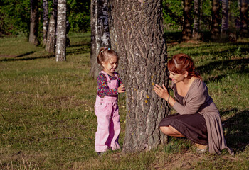 Middle aged woman playing with little girl hiding behind tree