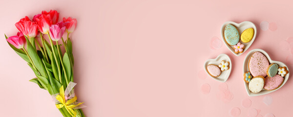 Happy Easter. Multi-colored pastel easter cookies gingerbread, seasonal flowers tulips on pink background. Easter concept, copy space, flyer, banner, coupon, greeting card, invitation