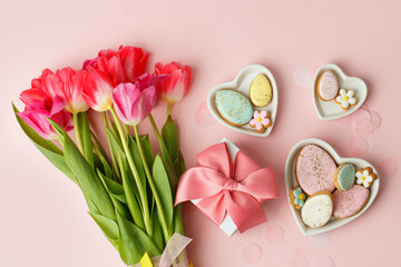 Happy Easter. Multi-colored pastel easter cookies gingerbread, gift box seasonal flowers tulips on pink background. Easter concept, copy space, flyer, banner, coupon, greeting card, invitation