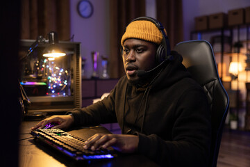 Shocked male professional computer gamer opens mouth looking at computer screen, talks to team through headset, presses buttons of backlit keyboard. Dark room lit by purple led light. © ABCreative