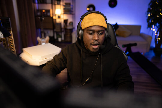 The man, seeing the opponents in the online game, faintly opened his mouth in shock. A professional gamer wearing a headset spends free time playing games. A mess in a man's room lit by led lights.
