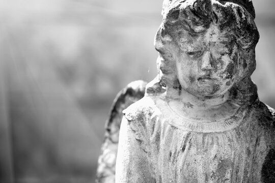 Praying angel with sweet facial expression. Black and white image of an ancient stone statue. Copy space.